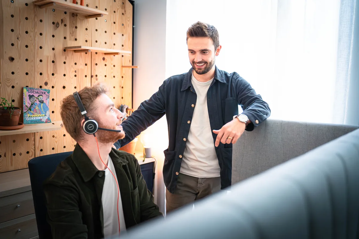 Manager commercial échangeant avec un commercial équipé d'un casque, à son poste de travail